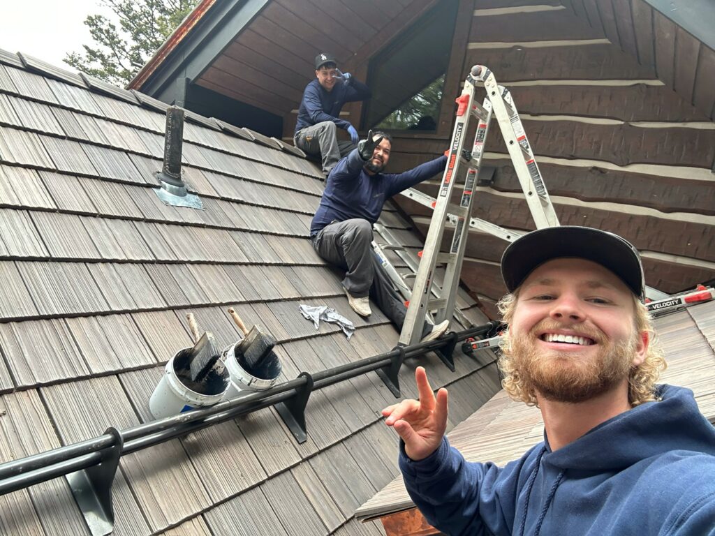 Log Care crew working from ladders along the roofline of a log home during a restoration